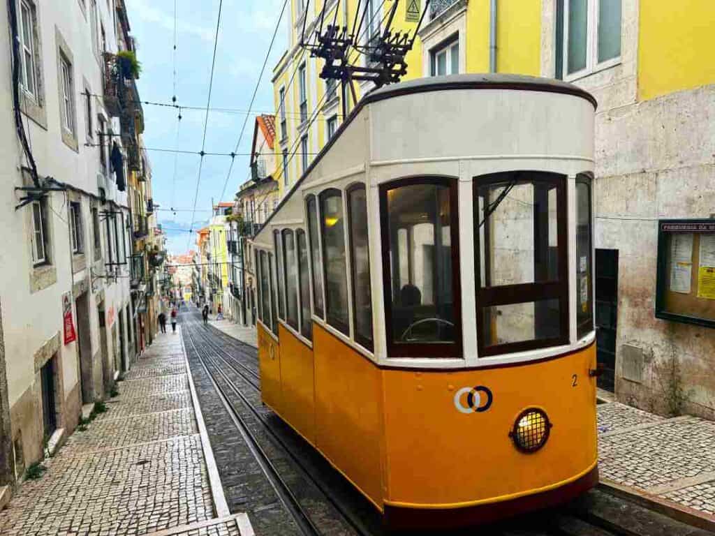 A yellow funicular on top of a steep, cobblestoned narrow street surrounded by old colonial brick buildings