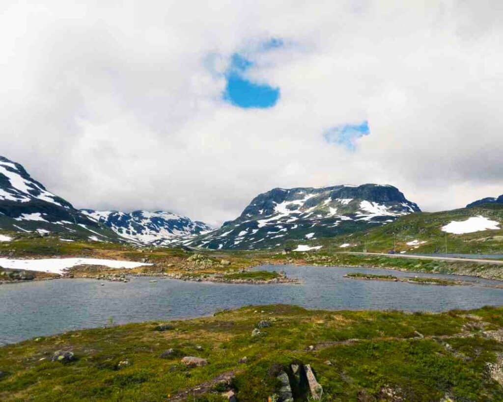 A mountain plain with green fields and snow patched mountains in the background