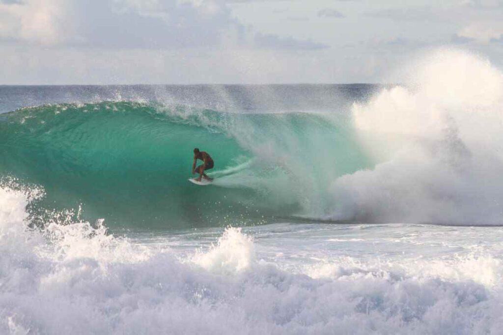 A surfer in the middle of a huge wave tunnel in green tropical water with whitewater on all sides