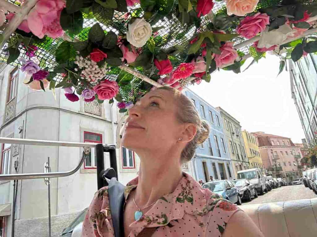 a woman sitting in a tuk-tuk, with a carpet of colorful flowers in the ceiling, driving along city streets