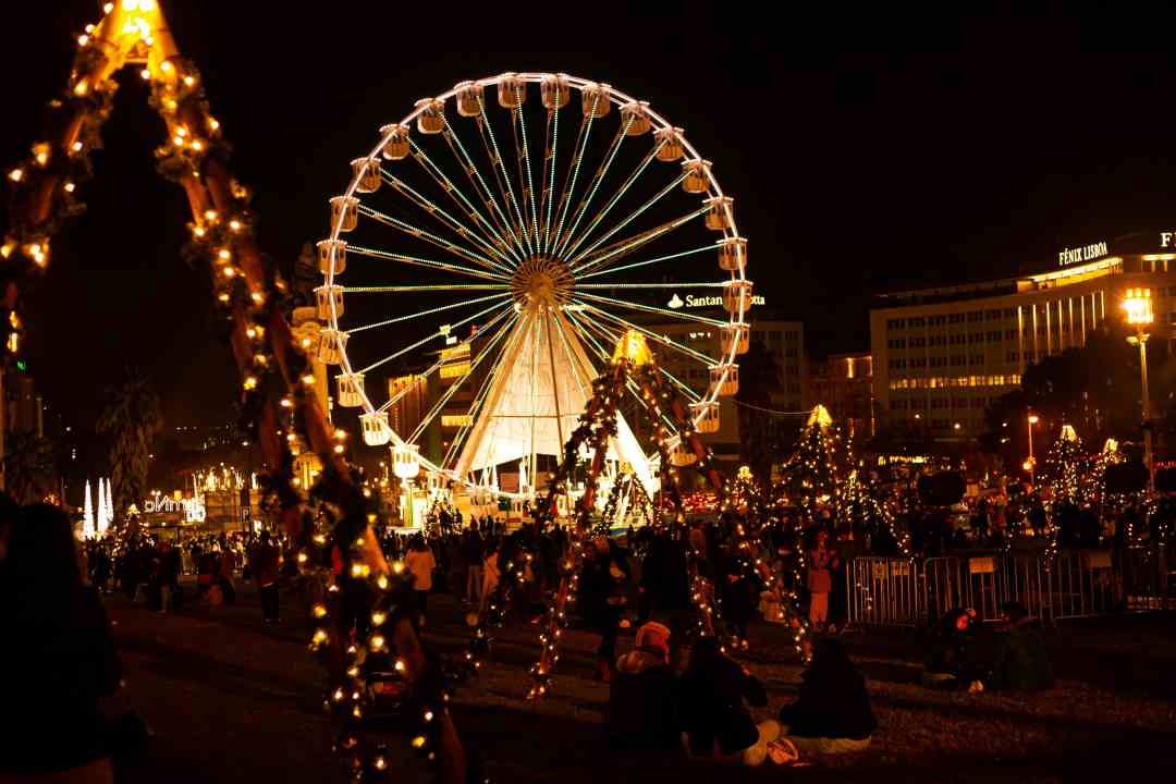 A ferris wheel at night surrounded by christmas decorations and people in a city square