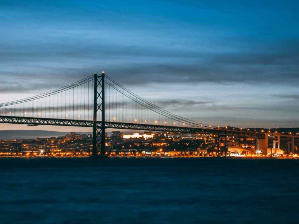 A majestic bridge at night over water with city lights in the background 