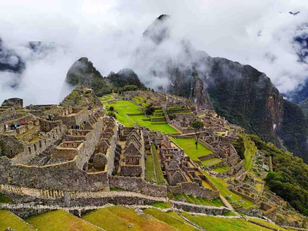 Old stone ruins in the mountains with green patches here and there, and floating mist around the mountain peaks