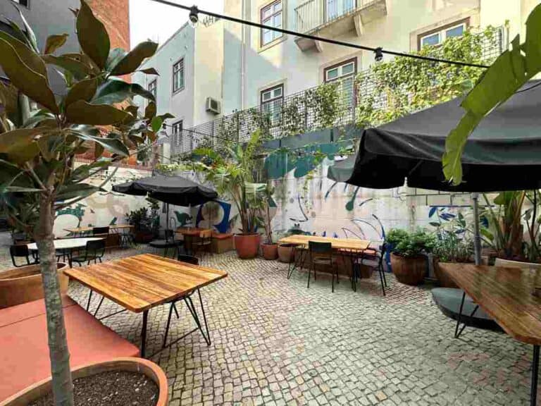 A cobblestoned backyard wtht nice seating areas, parasols, and grenery