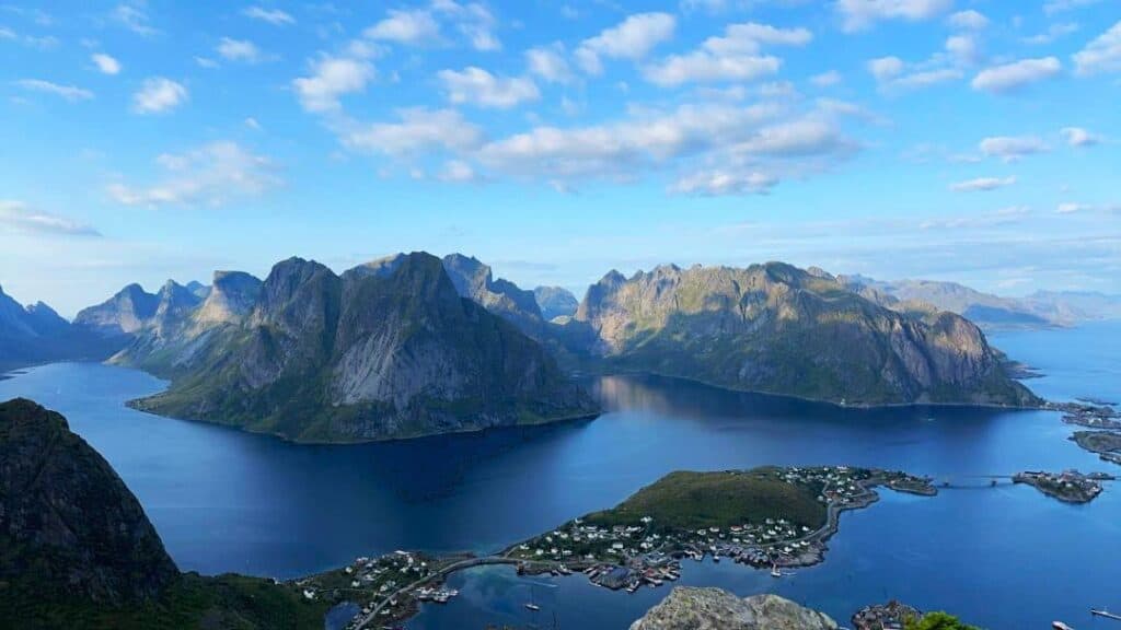 Majestic Arctic mountains steeping into the dark fjords under a blue sky, with a small village on an island in front