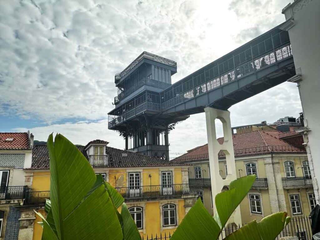 A grey iron structured walkway and tower over classic colonial buildings with a walkway over to a viewpoint above the city