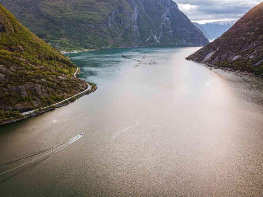 A spectacular narrow fjord winding into the mountains with steep mountain sides on either side of the body of water, and a small boat sailing on the water