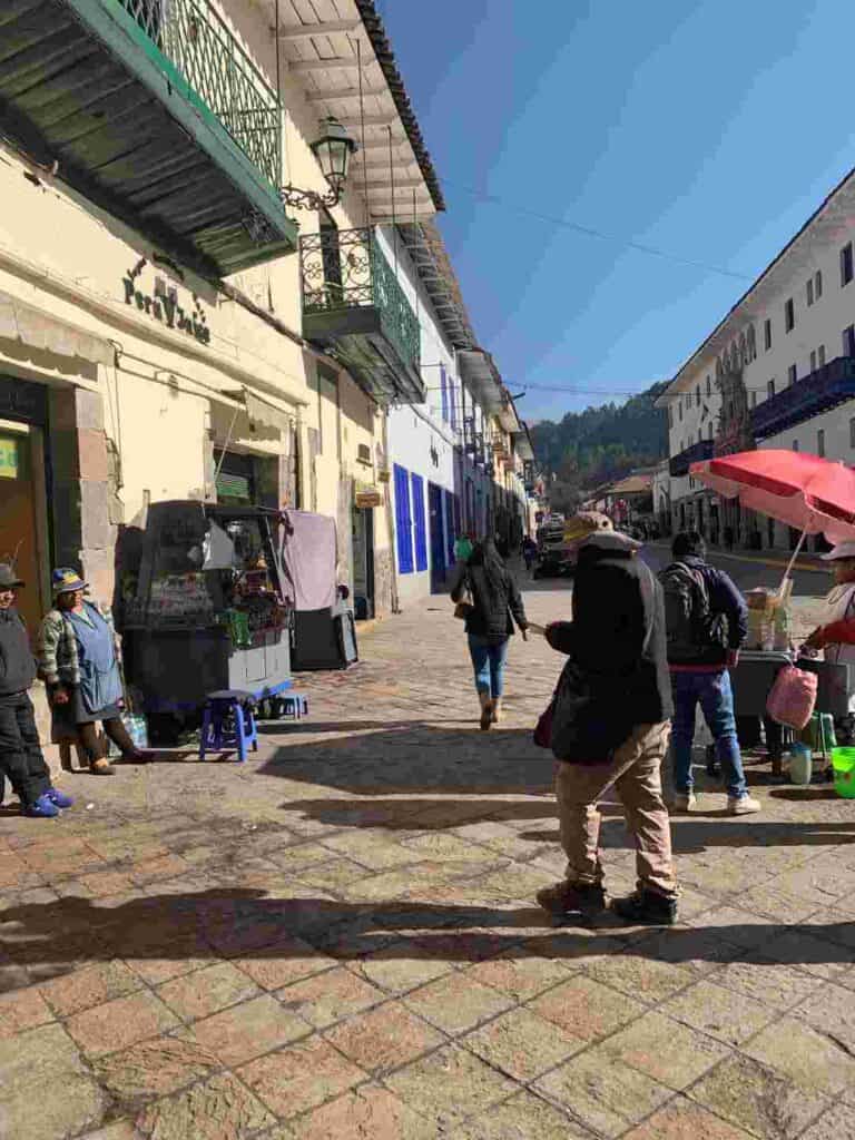 Street ambiance from a mountain town with people strolling, venders selling in between light colored brick houses with beautiful colored details on a sunny day