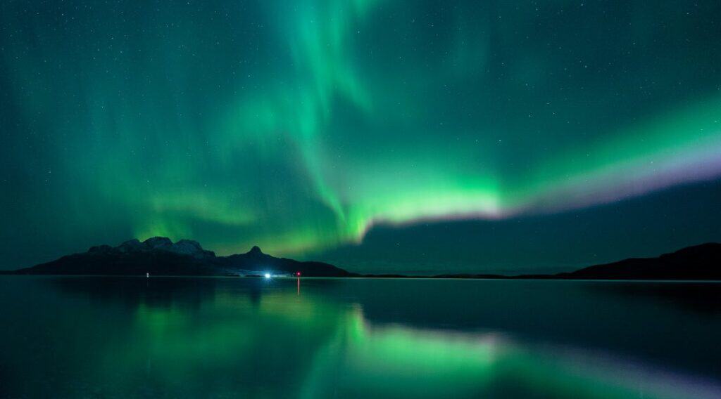 Shades of deep green northern lights floating across the dark winter sky reflected in the dark waters of the Arctic 