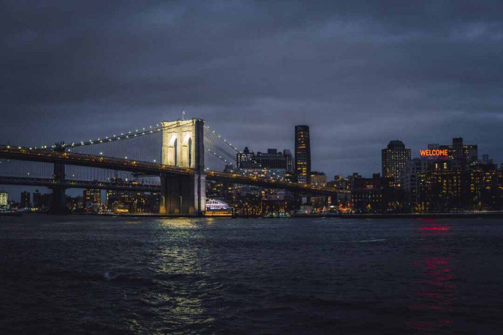 A beautiful old bridge lit at night over dark water with a backdrop of a city skyline