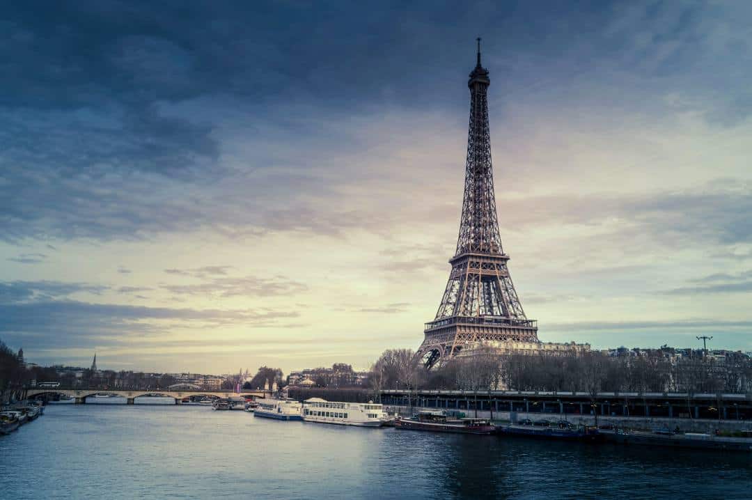 The Eiffel Tower in France with its tall iron structure against a pale sunset in winter across the river Seine