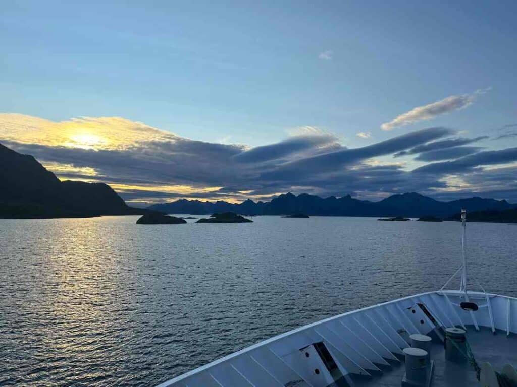 stunning views of the blank sea and the sunset in the distance behind dark remote islands seen from the white bau of a ship