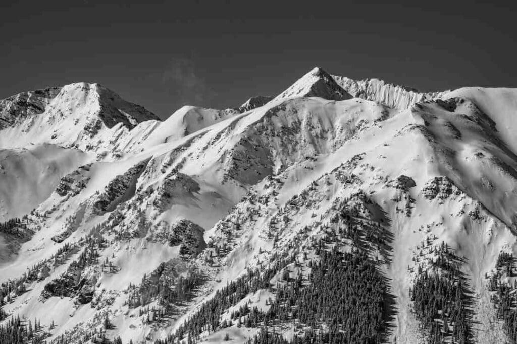 A vast mountain with peaks and gorges covered with snow and trees in the lower areas that looks perfect for off pist skiing