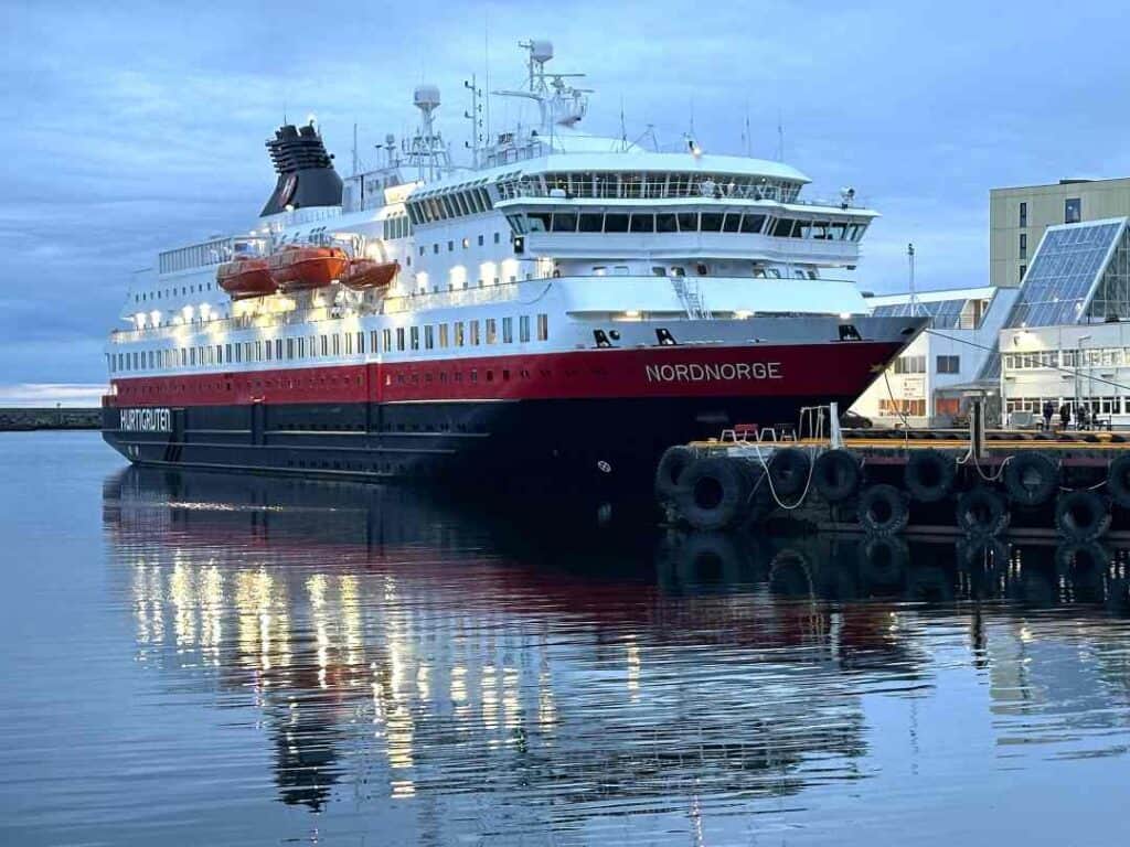 Red, white and black small cruise ship in port in an Arctic town at dusk