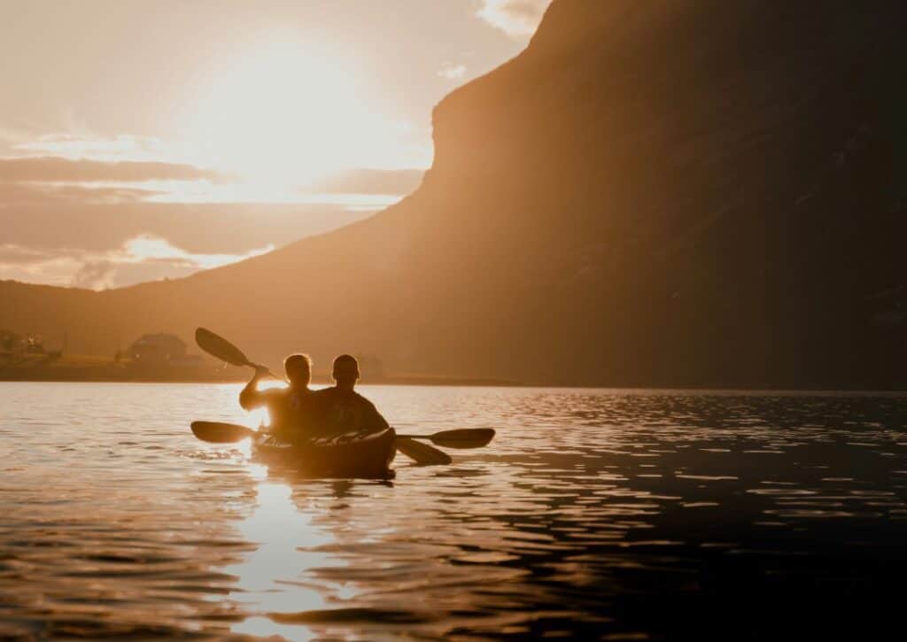 Two people in a kayak on the blank sea under a mountain and glowing golden light from a low sun