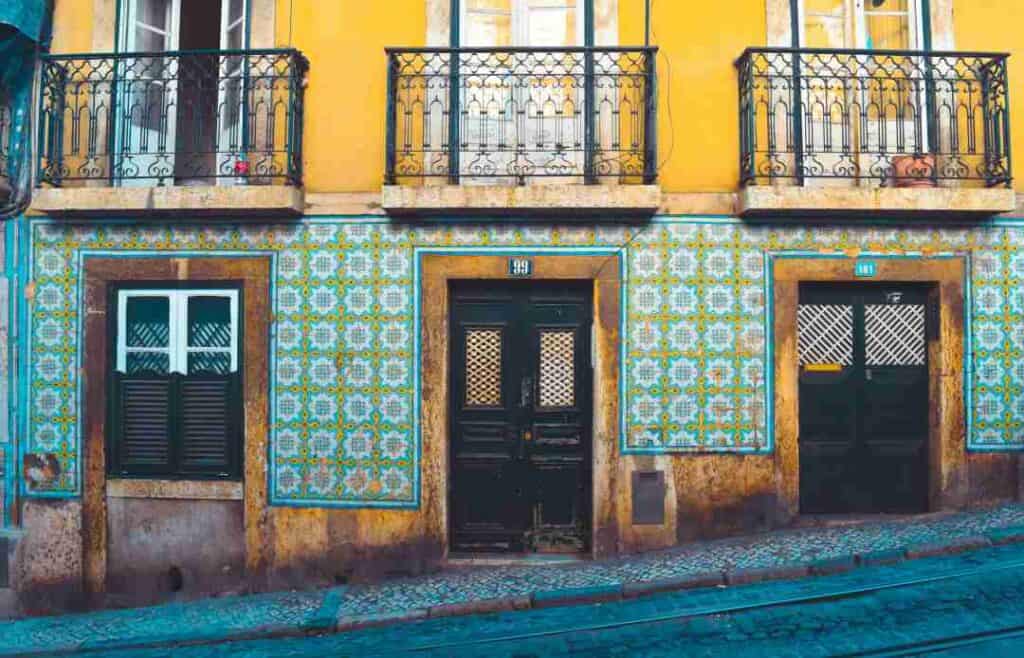 The facade of a colonial building decorated with beautiful blue tiles on the first floor, with elaborately decorated windows, under the yellow painted second floor where every window has a little balcony