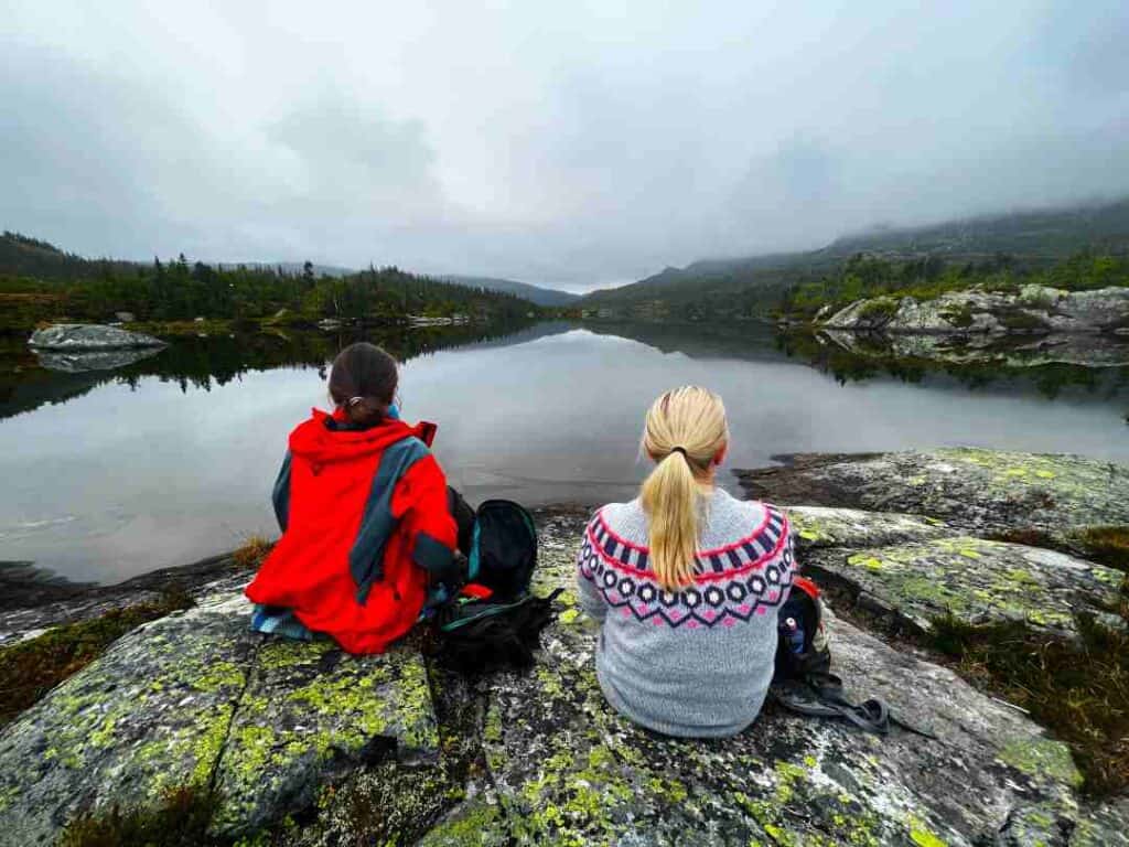 Two women sitting on a rock gaizing over a blank mountain lake on a misty cloud covered day