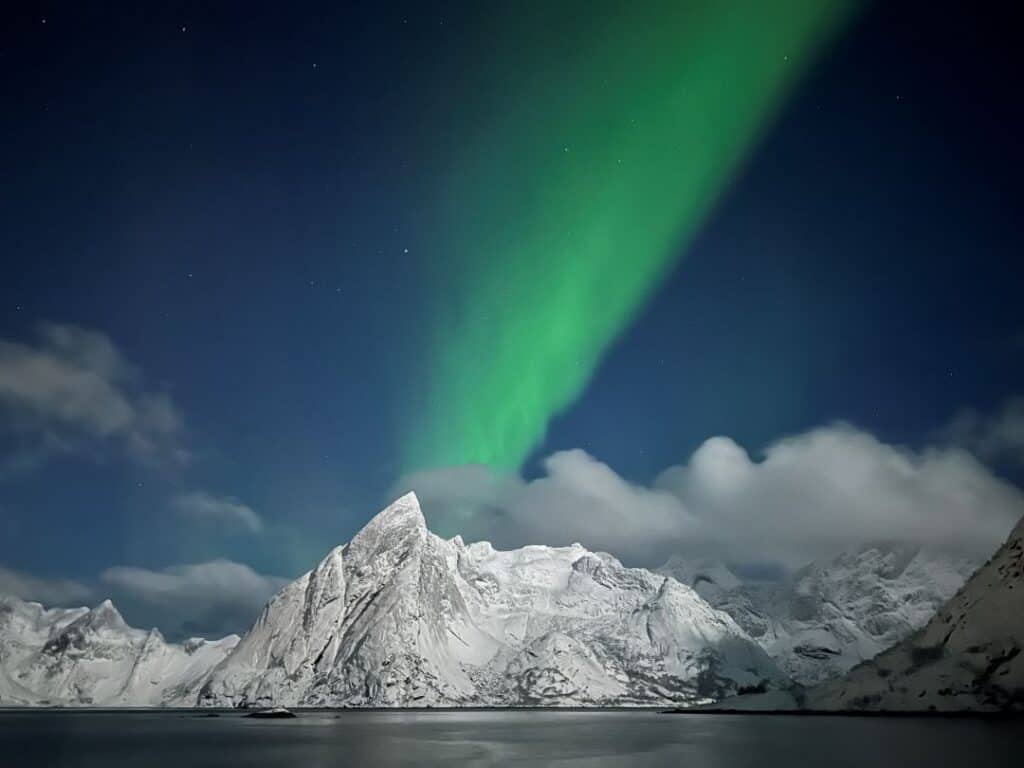 Green beautiful northern lights in a deep blue sky over white snow covered mountains