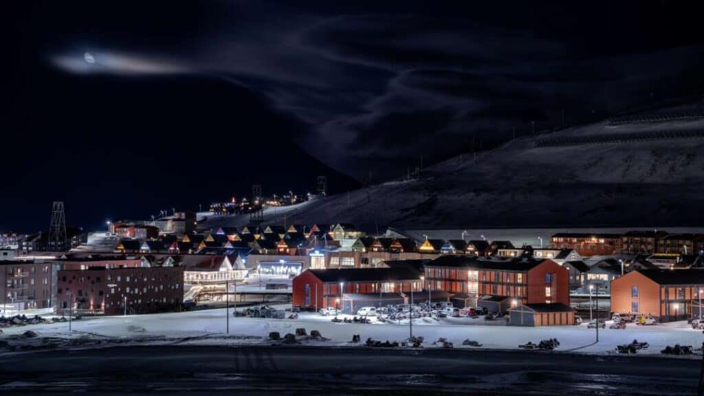 A small town or settlement with lots of lights from the city in overall winter darkness under a dark sky, during the Polar Night in the arctic