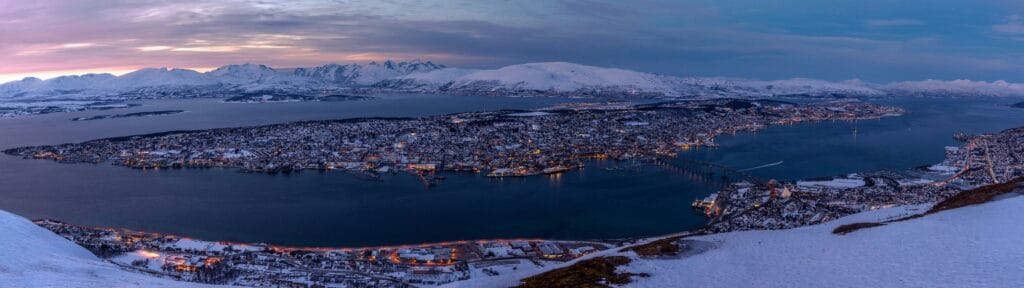 A town situated on an island in the Arctic blue lights seen from a viewpoint with snow covered moutnains in the distance