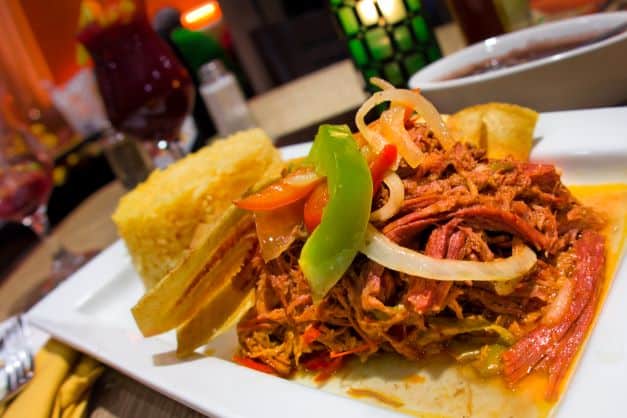 A white plate with a delicious looking dish withe schredded meat and vegetables, and rice on the side