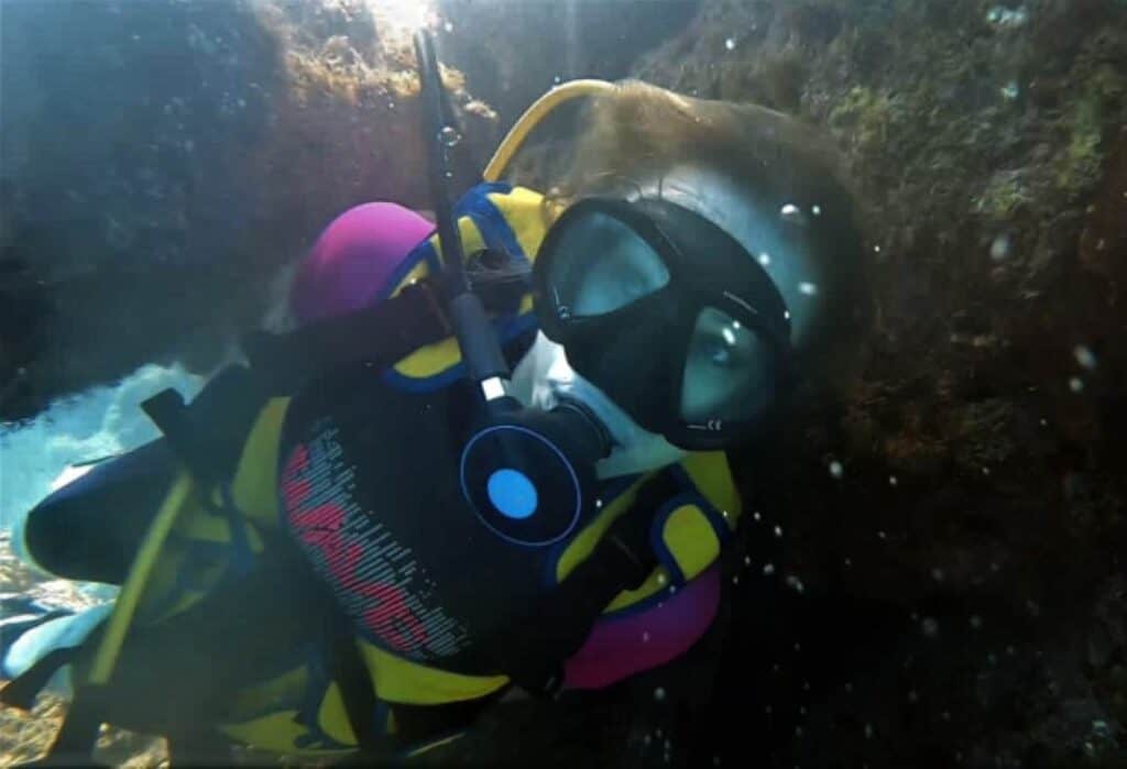 Close up photo of a woman scuba diving, wearing a pink and yellow suit swimming through underwater nature