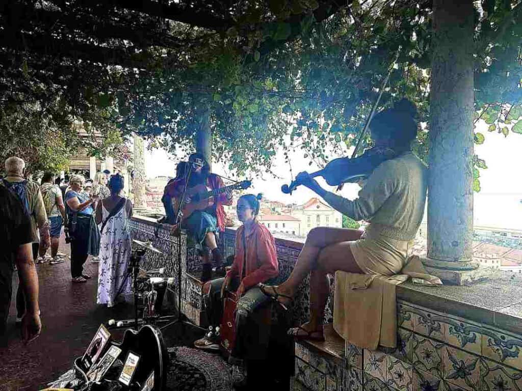 A woman playing the violin on a viewpoint high above a city, with lots of people around her