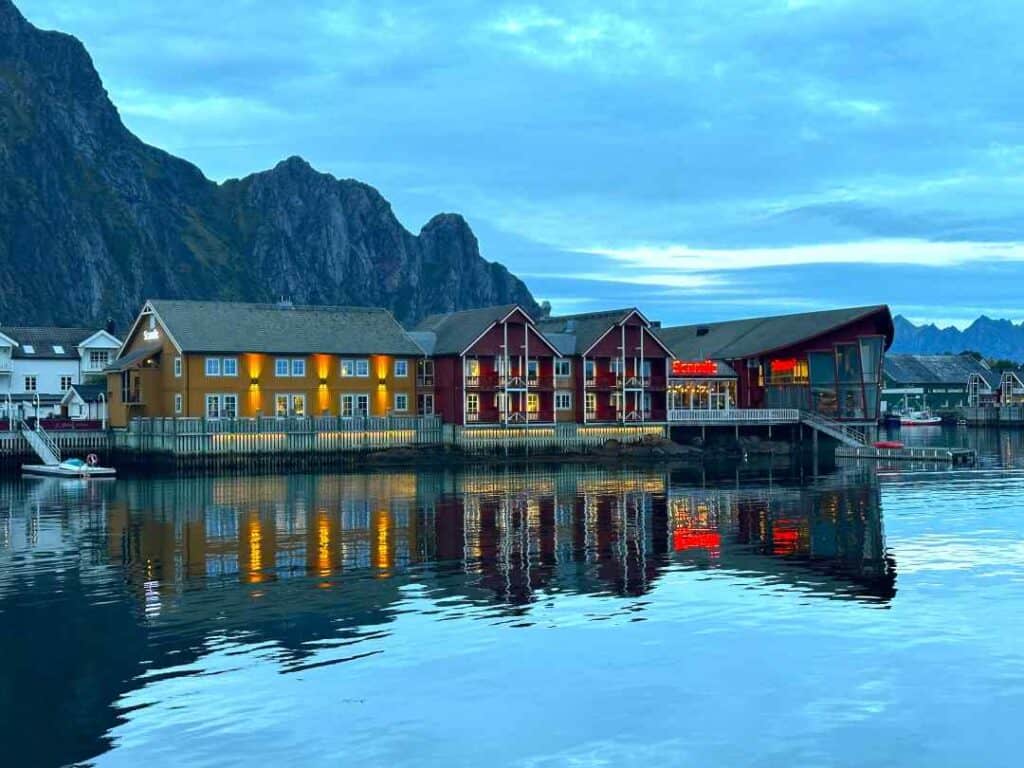 Charming old wooden houses in bright strong colors an afternoon at dusk by the blank water with majestic mountains in the distance