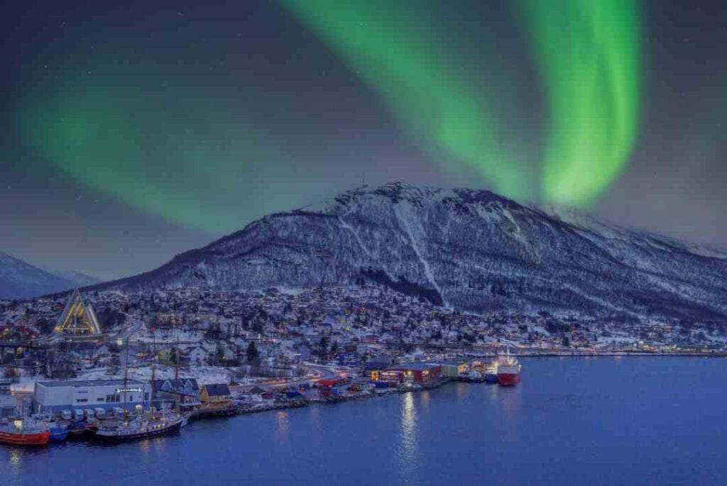 Northern lights on the night sky over a snow covered mountain and a town by the sea