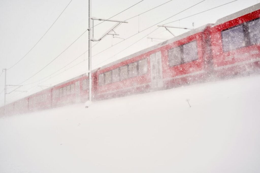 A red train in a snow storm covered by snow evertwhere