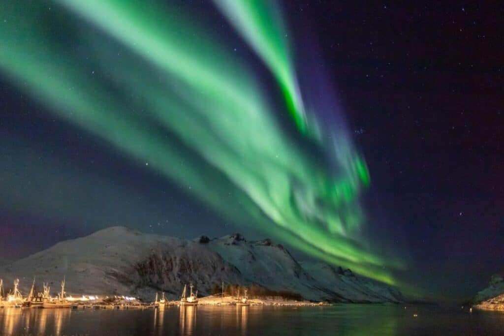 Green Northern lights dancing on the dark sky over a snow covered mountain and the blank sea