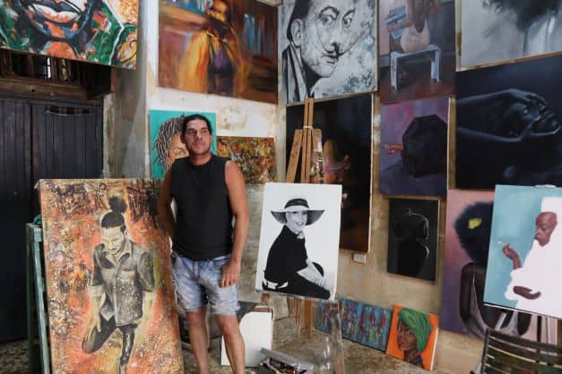 An artist in his studio surrounded by his colorful art on the walls and the floor