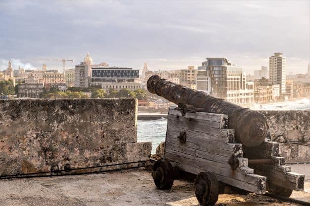 An old cannon on wooden wheels pointed out towards a bay, where it used to be the city protection for a Caribbean capital