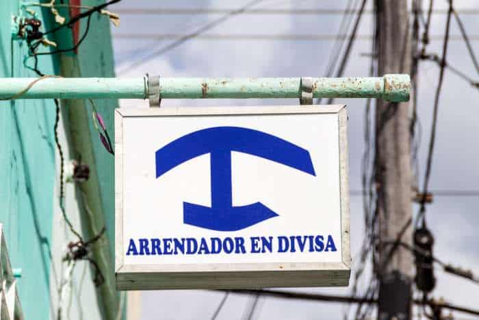 A blue big T on a white background on a sign hanging on a brick wall