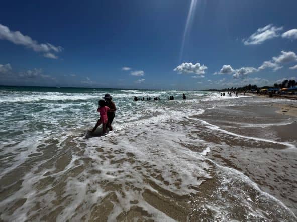 a golden sandy beach on a Caribbean island under a clear blue sky with soft waves washing over the sands and children playing in the waves