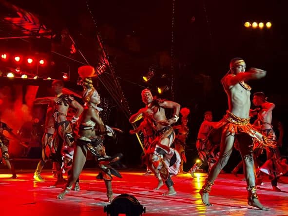 Energetic dancers on stage in a red light, wearing indigenous costumes from the Caribbean, putting on a fast and furious show